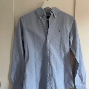 Blå skjorta från Ralph Lauren - Snygg skjorta från Ralph lauren som tyvärr måste säljas för den inte passar . Ny skick och använd fåtal gånger med inga defekter. Snabb frakt och pris inte hugget i sten skriv om frågor🤩🤩
