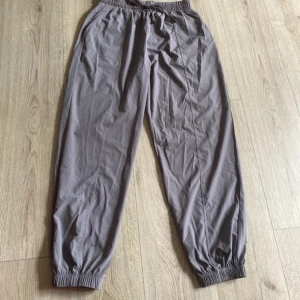 Grå mjukisbyxor i polyester - Säljer ett par grå mjukisbyxor i storlek M. De är tillverkade av 100% polyester och har en elastisk midja för extra komfort. Perfekta för en avslappnad dag hemma eller en promenad i parken. Byxorna har resår vid anklarna för en snygg passform.