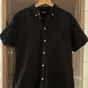 Svart kortärmad skjorta från WeSC - Säljer en stilren svart kortärmad skjorta från WeSC. Sitter snyggt boxy, I nyskick.