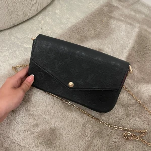 Svart kuvertväska med kedja - Säljer en elegant svart kuvertväska med en snygg guldkedja. Perfekt för festliga tillfällen eller en utekväll men även vardag. Den stängs med en knapp och har plats för det viktigaste.