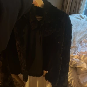 Svart pälsjacka från Vila - Säljer en superfin svart pälsjacka från Vila i storlek M. Den är perfekt för både höst och vinter och ger en lyxig känsla. Jackan har långa ärmar och är i nyskick. Den är både varm och stilren, perfekt för att höja din outfit till nästa nivå!