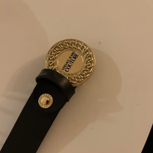 Versace bälte  - Versace bälte i guld och svart. 3 egna hål gjorda i bältet, se bild.