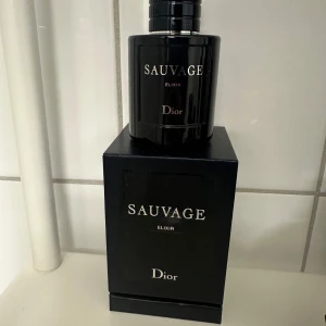 Sauvage Elixir från Dior - Säljer en elegant och intensiv parfym, Sauvage Elixir från Dior. Flaskan är mörk och stilren med en svart glansig yta och silverdetaljer. Perfekt för den som söker en kraftfull och sofistikerad doft.