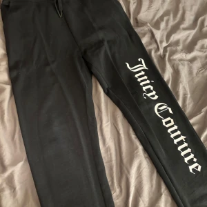 Svarta mjukisbyxor från Juicy Couture - Snygga svarta mjukisbyxor från Juicy Couture med stort tryck längs benet. Perfekta för en avslappnad stil med elastisk midja och dragsko för bästa passform, fickor på sidorna. Lite använda storlek small 