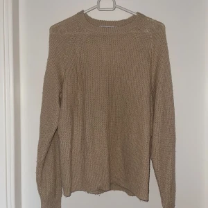 Beige stickad tröja från NA-KD - Säljer en stilren beige stickad tröja från NA-KD. Perfekt för kyligare dagar med sin mjuka och bekväma passform. Tröjan har långa ärmar och en rund halsringning. Ett måste i garderoben för en avslappnad look.