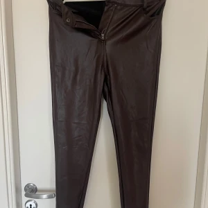 Bruna skinnleggings från FB Sister - Snygga bruna skinnleggings från FB Sister i storlek S. De har en tight passform med dragkedja och knapp framtill. Perfekta för en trendig look.