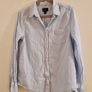 Ljusblå skjorta från Gant - Snygg ljusblå skjorta från Gant med klassisk krage och knappar framtill. Skjortan har en bröstficka och långa ärmar med manschettknappar. Perfekt för en stilren look.