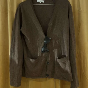 Brun kofta från Hope - Säljer en brun kofta från Hope med v-ringning och knappar framtill. Koftan har långa ärmar och två praktiska fickor. Perfekt för lager-på-lager under kyligare dagar. Skick 7/10 och storleken är S. Tveka inte att skriva vid frågor eller funderingar!