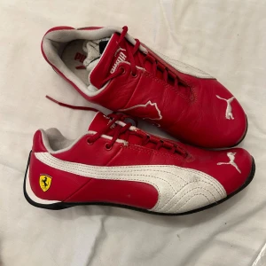 Röda Puma sneakers med Ferrari-logga - Snygga vintage röda Puma sneakers med vit detaljering och Ferrari-logga på sidan. Skorna har snörning och är tillverkade i syntetmaterial.