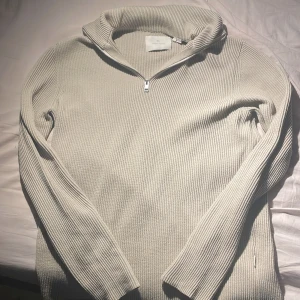 Beige ribbad tröja från Jack & Jones - Säljer en stilren beige ribbad tröja från Jack & Jones. Tröjan har en dragkedja vid halsen och långa ärmar, perfekt för kyligare dagar. Passar både till vardags och mer avslappnade tillfällen.