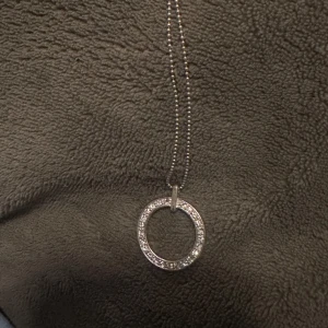 Silverfärgat halsband med cirkelberlock - Elegant halsband med en glittrande cirkelberlock i silverfärg. Kedjan är tunn och smidig, vilket ger ett stilrent intryck. Perfekt för att lägga till en touch av elegans till din outfit.