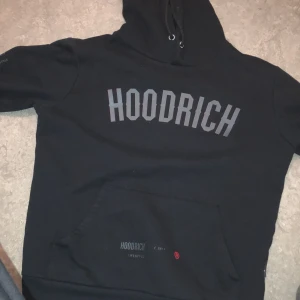 Svart hoodie från Hoodrich - Säljer en svart hoodie från Hoodrich med tryck på både framsidan och baksidan. Den har en stor ficka framtill och justerbar huva med dragsko. Perfekt för en avslappnad stil.