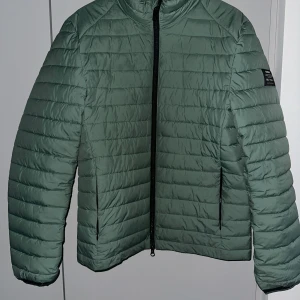 Jacka från ecoalf  - Snygg grön jacka från ecoalf. Jackan har en stilren design och en bekväm passform. Perfekt för kyligare dagar.  