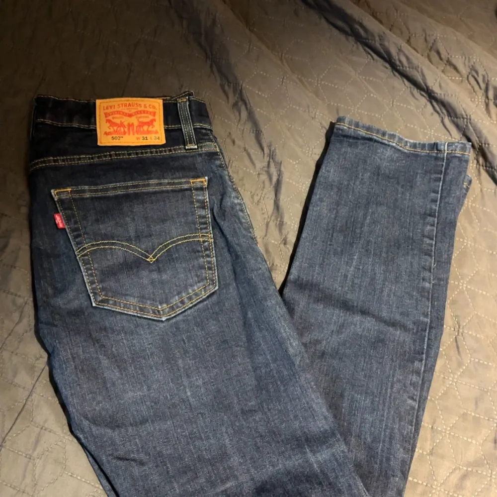 Snygga Levis 502 jeans i klassisk blå denim. De har en straight passform och är perfekta för en avslappnad stil. Jeansens ikoniska läderpatch och kontrastsömmar ger en tidlös look. L: 105, B: 45. Farkut & Housut.