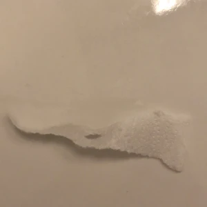 Pappers bit - Bilderna visar en vit yta med ojämna, rivna kanter. Det ser ut som papper eller en liknande tunn, vit materialbit som har fastnat eller applicerats på en slät yta. Detaljer om material eller kontext är begränsade.