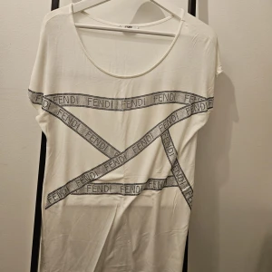 Vit topp från Fendi - Snygg vit topp från Fendi med svart logotypmönster i form av band som korsar varandra på framsidan. Toppen har en rund halsringning och korta ärmar. Perfekt för en stilren look.