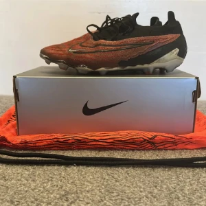 Nike Phantom GT fotbollsskor Elite - Säljer ett par Nike Phantom GT fotbollsskor i svart och orange. Skorna har en snygg design med snörning och är perfekta för fotbollsspelare som vill ha bra grepp och kontroll på planen.