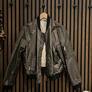 Grön bomberjacka från Zara Basic - Snygg grön bomberjacka från Zara Basic med dragkedja och fickor. Jackan har en klassisk bomberstil med ribbade muddar och krage. Perfekt för en cool och avslappnad look.