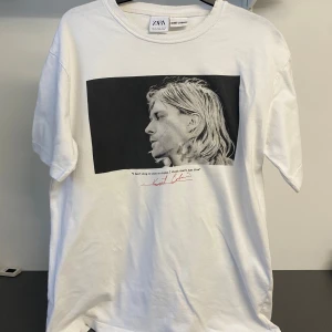 Vit t-shirt med Kurt Cobain-tryck från Zara - Snygg vit t-shirt från Zara med ett stort tryck av Kurt Cobain på framsidan och hans namn i rött på baksidan. Citatet 'I can't sing or play or rhyme, I think that's just fine' finns under bilden. Perfekt för fans av rockikoner! Tror storleken är fel markerad eftersom den är väldigt stor. Kan vara storlek M