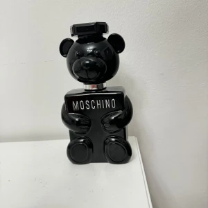 Svart parfymflaska från Moschino - Unik parfymflaska i form av en svart björn från Moschino. Flaskan har en glänsande finish och är både lekfull och stilren. Perfekt för den som vill ha en iögonfallande detalj på sminkbordet. Använd några gånger men var inte min smak. Ca 90 % av parfymen kvar