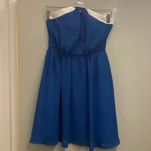 Blå axelbandslös finklänning - Kort blå finklänning i chiffong, köpt på Nelly. Har inga axelband utan ett band från mitten som man kan knyta som man vill, eller ta bort.