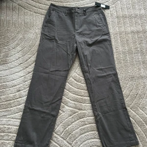 Grå kostymbyxor HELT NYA!! - HELT NYA!! Snygga grå kostymbyxor med rak passform och diskreta fickor. Perfekta för en stilren look. Byxorna har hällor för bälte och en klassisk design. 