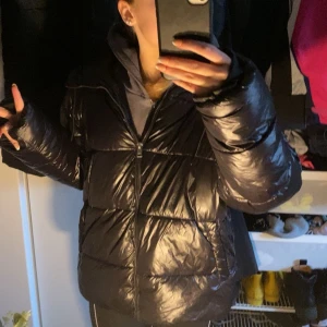 Svart pufferjacka - Säljer en svart pufferjacka med dragkedja. Jackan har en glansig yta och långa ärmar, perfekt för kyliga dagar. Den är både stilren och praktisk. Köpt från Lager 157 och är i storlek M, men tycker den sitter ganska bra på mig som bär xs/s, superfint skick!💕