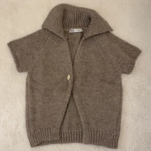 Beige stickad kofta från Zara - Säljer en beige stickad kofta från Zara med korta ärmar och en stor krage. Koftan har en knapp framtill och är croppad, vilket ger en trendig look. Perfekt för lager-på-lager-stil. (Säljer för intressekoll)💞💞