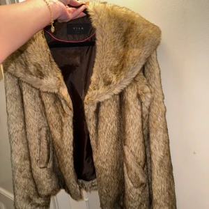 Beige pälsjacka från Vila - Snygg beige pälsjacka från Vila med mjukt foder och stor krage. Perfekt för att hålla sig varm och stilren under kyliga dagar. Jackan har en elegant design och passar bra till olika outfits. I fint skick, köpt för 999kr 