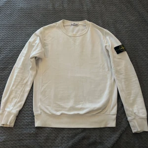 Vit tröja från Stone Island - Säljer en stilren vit tröja från Stone Island med deras ikoniska märke på ärmen. Tröjan är sparsamt använt och har inga defekter.