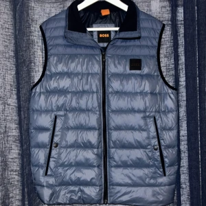Blå dunväst från BOSS - Snygg blå dunväst från BOSS med dragkedja och hög krage. Perfekt för lite kyligare dagar!  (Bra skick, använt en eller två gånger) 