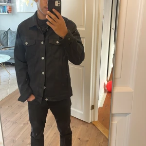 Svart overshirt från Jack&Jons - Snygg svart overshirt från jack&Jons med silverfärgade knappar. Jackan har två bröstfickor med lock och knappar samt två fickor 