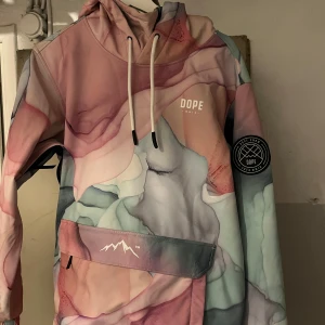 Flerfärgad jacka från Dope Snow - Säljer en cool flerfärgad jacka från Dope Snow med ett abstrakt mönster i rosa, blått och grönt. Jackan har en stor ficka med dragkedja framtill och en justerbar huva med snören. Perfekt för dig som vill sticka ut i backen! finns att hämta i indal annars går det att mötas upp kring sundsvall eller postas!