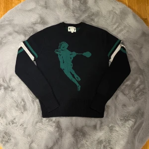 Stickad tröja från GANT - Snygg svart stickad tröja från GANT med grönt motiv på framsidan. Tröjan har långa ärmar med vita och gröna ränder samt en rund halsringning. Väldigt skönt material som värmer bra under vintern. Perfekt för en stilren look. 