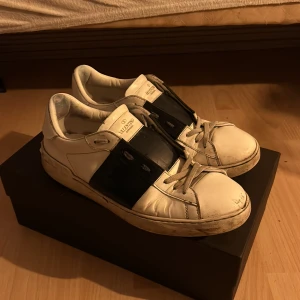 Valentino Open sneakers i vitt och svart - Snygga Valentino Open sneakers i vitt med en bred svart rem över snörningen. Skorna har en klassisk design med en modern twist och är perfekta för en stilren look. Allt og medföljer och äktighets bevis finns. Pris är ej hugget i sten😁 Tar emot byten med👍