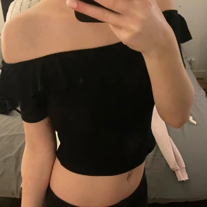 Svart offshoulder topp från Zara - Snygg svart offshoulder topp från Zara med volangdetaljer. Perfekt för en stilren look. Toppen är croppad och ger en trendig touch till din outfit. Den är i storlek m men sitter som S