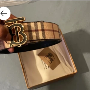 Rutig bälte från Burberry - Säljer ett stilrent bälte från Burberry med klassiskt rutigt mönster i beige och bruna toner. Bältet har ett elegant guldfärgat spänne med Burberrys ikoniska logotyp. Perfekt för att lyfta vilken outfit som helst.