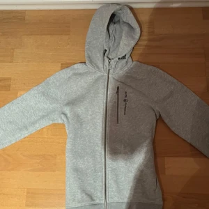 Grå hoodie från Sail Racing - Tja! Säljer denna grå hoodie från Sail Racing med dragkedja och huva. Säljer den då jag har växt ut den. Inga defkter och knappt använd, så gott som ny. Ny pris 1500kr ( obs priset är inte hugget i sten)