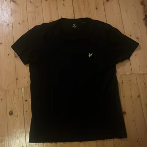 Svart t-shirt från Lyle & Scott - Snygg svart t-shirt från Lyle & Scott med korta ärmar och en liten gul logga på bröstet. Perfekt för en stilren look.