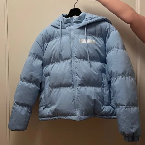 Ljusblå pufferjacka från Hoodrich - Säljer en ljusblå pufferjacka från Hoodrich med huva.. Använd en gång.