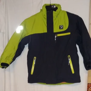 Svart och limegrön jacka med reflexdetaljer - Säljer en svart och limegrön jacka från gneis med praktiska reflexdetaljer. Jackan har dragkedjor i kontrasterande färg och flera fickor för förvaring. Plus att de är magnetknappar. Perfekt för utomhusaktiviteter med sin funktionella design.