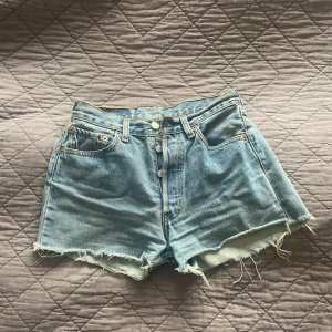 Blå jeansshorts från Levi's - Levisshorts i modellen 501, köpta second hand. Skicket är använt (se sista bilden med lappen som är lite sliten). Sitter väldigt fint på. Storleken är w28 - de kommer att passa bra om du har stl xs-s. 