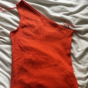 Orange oneshoulder topp från Ullared - Snygg orange oneshoulder topp från Ullared i ribbat material. Perfekt för en trendig look med sin unika asymmetriska design. Eller varför inte göra den till en orange crop top?Storlek M (40-42).
