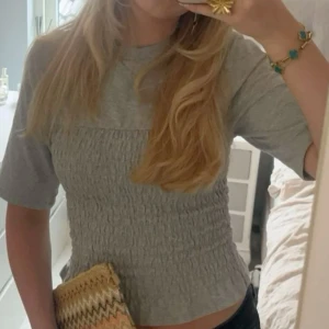 Grå ribbad topp - Säljer en stilren grå ribbad topp med trekvartsärm och volangdetalj vid nederkanten. Perfekt för en avslappnad look.