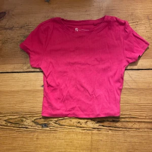 Rosa ribbad topp från FSBN Sister - Snygg rosa ribbad topp från FSBN Sister i storlek S. Denna kortärmade topp har en croppad passform och är perfekt för en trendig look. Tillverkad i ett mjukt och bekvämt material.