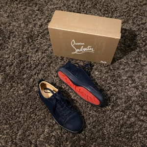 Marinblå sneakers från Christian Louboutin - Snygga marinblå sneakers från Christian Louboutin med den ikoniska röda sulan. Skorna har snörning och är tillverkade i ett elegant material som ger en lyxig känsla. Perfekta för att ge din outfit en exklusiv touch. Storleken är 41 men passar även för 42! 