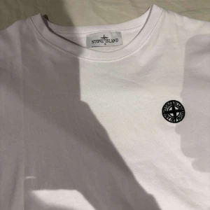  Stone Island - Snygg vit t-shirt från Stone Island med rund hals och korta ärmar. Den har en broderad logotyp på bröstet. Perfekt för en stilren look.