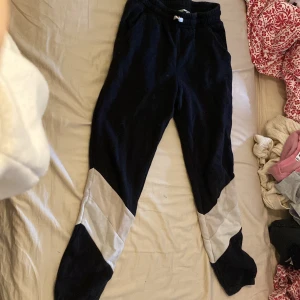Svarta mjukisbyxor från H&M - Säljer ett par svarta mjukisbyxor från H&M i storlek 152. Byxorna har vita detaljer på benen och är perfekta för en avslappnad stil. De är gjorda i ett mjukt material som är skönt att ha på sig. Perfekta för mysiga dagar hemma eller en chill dag ute.