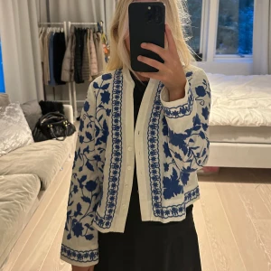 Vit och blå broderad jacka från Zara - Säljer en superfin vit jacka från Zara med blått blommönster. Den har långa ärmar och knappar framtill. Perfekt för vår och sommar när du vill ha något lätt men ändå stiligt. Jackan är i bra skick och passar perfekt till både vardag och fest!