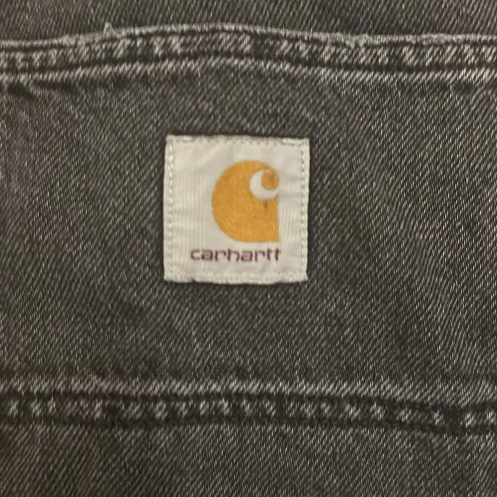 Säljer ett par svarta byxor från Carhartt. De har en robust design med förstärkta knän och en avslappnad passform. Perfekta för både arbete och vardag. Byxorna har en klassisk femficksdesign och en dragkedja i gylfen. . Jeans & Byxor.